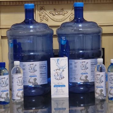 Bottles and large containers of Time 2 Alkaline water displayed on a reflective surface.