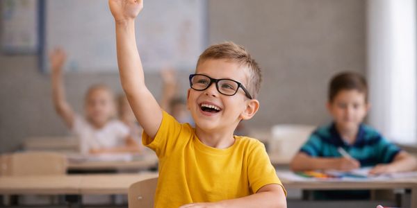 Smiling boy in glasses raising hand in classroom.