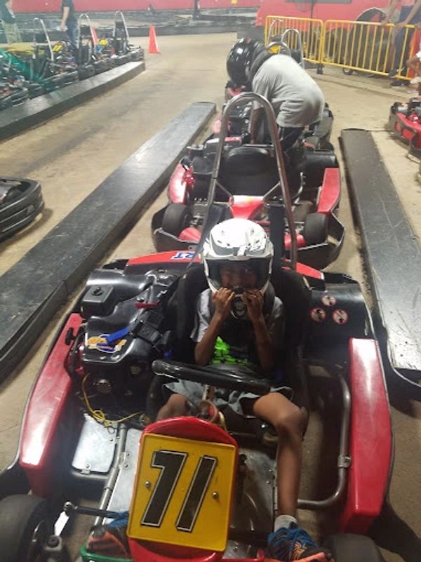 Happy young boy wearing a go-karting helmet getting ready to race at the indoor cart racing track.