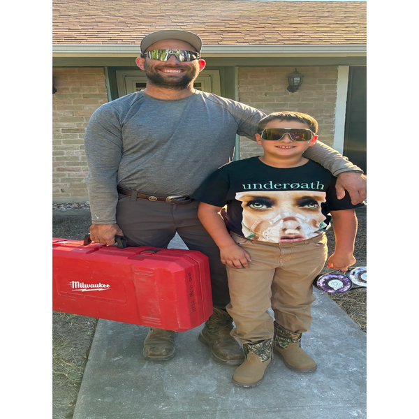 Man and boy wearing sunglasses, smiling outdoors with a red Milwaukee tool case.