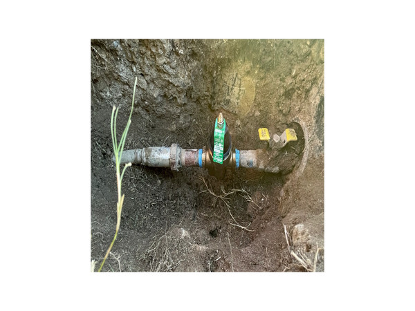 Exposed underground water meter and pipes in soil.
