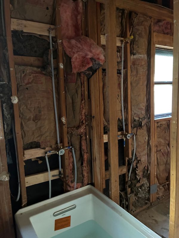 Partially demolished bathroom with exposed insulation and plumbing around a bathtub.