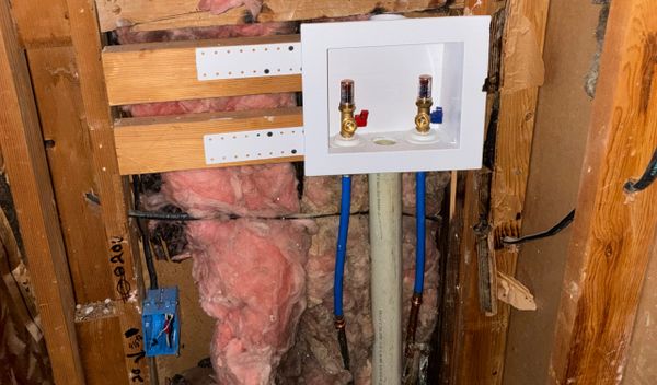 Laundry water supply valves installed in framed wall with pink insulation.