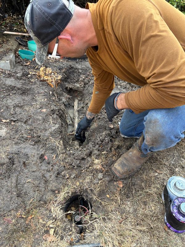 Man digging a trench to repair an underground pipe in a garden.