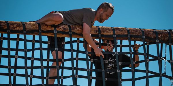 Man climbing over a net obstacle under clear blue sky.