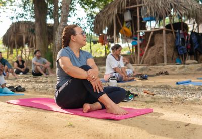 Persona sentada en colchoneta rosa haciendo yoga al aire libre.