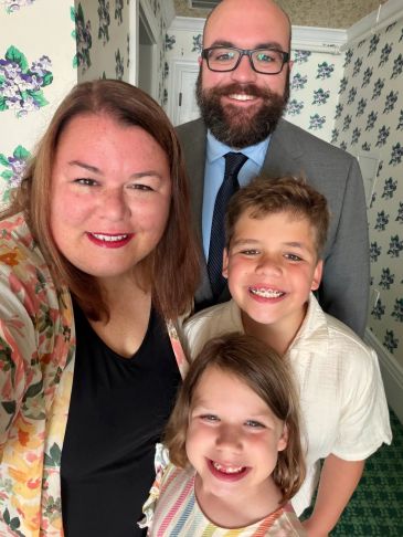 Family smiling indoors with floral wallpaper.