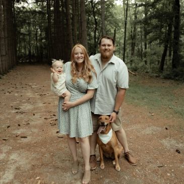Family portrait with couple, baby, and dog in forest.