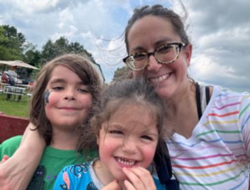 A smiling woman with two children outdoors.