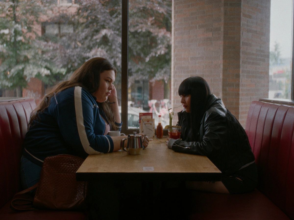 Two women sitting at a diner booth having drinks.