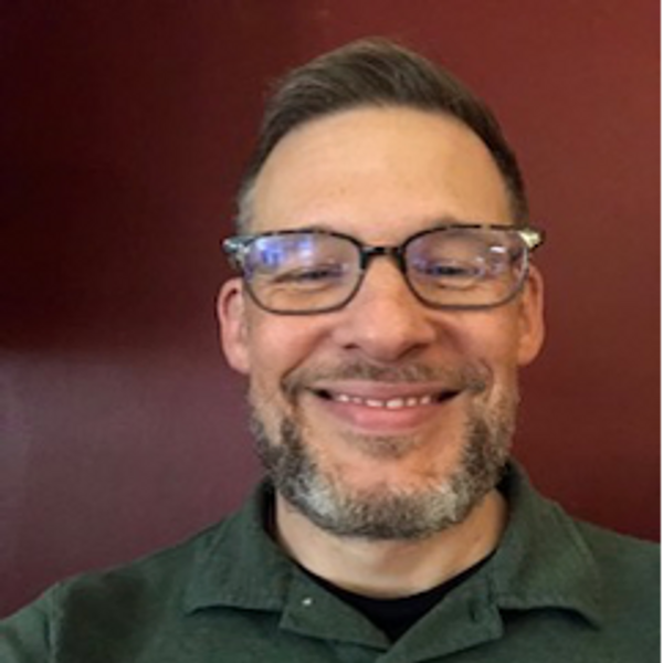 Smiling man with glasses and beard wearing a green collared shirt.