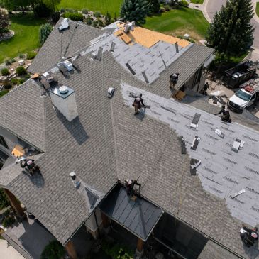 Workers installing roofing shingles on a large house.