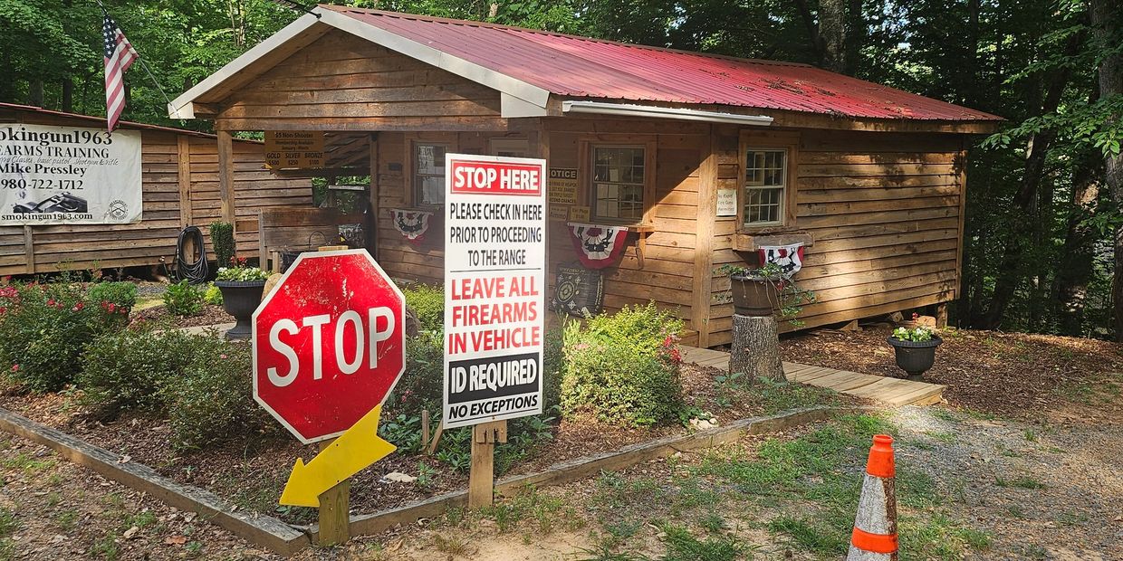 Entrance to a rustic shooting range with multiple stop signs and check-in instructions.