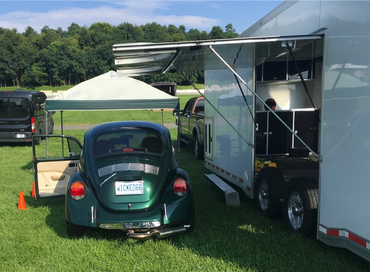 a green Volkswagen Bug beside an enclosed trailer