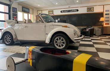 black soapbox derby car next to white Volkswagen