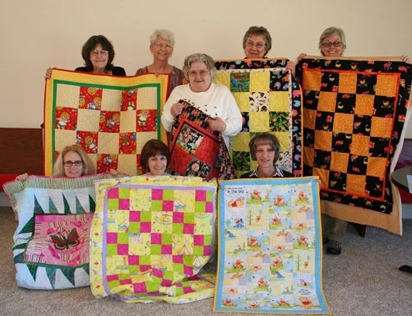 Group of women displaying colorful quilts.