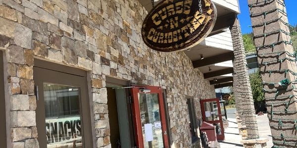 Stone building with a hanging wooden sign and snack shop window.