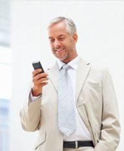 A man with gray hair, wearing e beige suit, white tie, and holding a phone