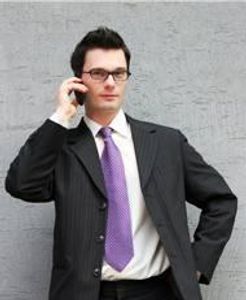 A man with black hair, wearing a purple tie, and has a phone
