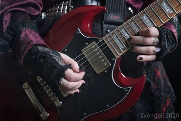 A pale woman with lace gloves plays a red SG guitar