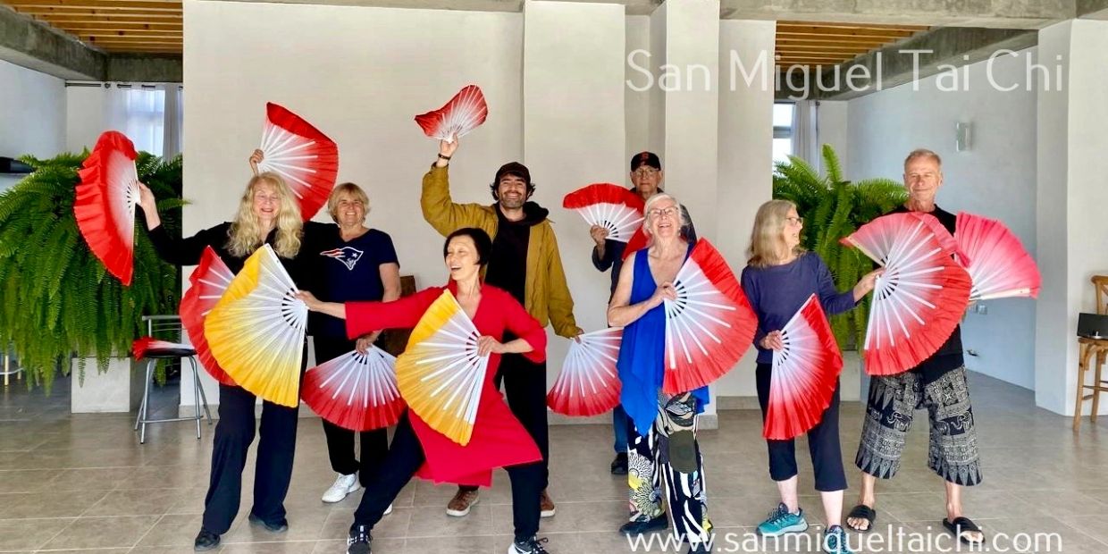 Group practicing Tai Chi with colorful fans indoors.