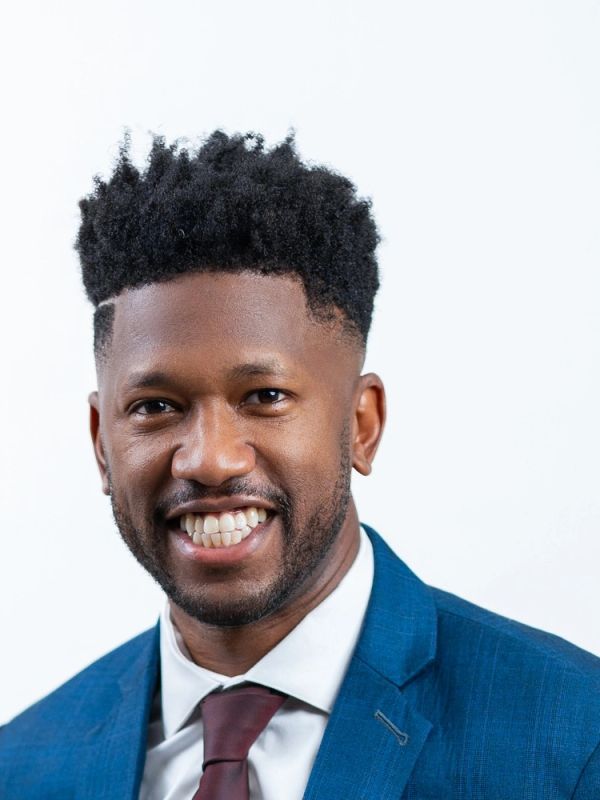 Smiling man in a blue suit and maroon tie against a white background.