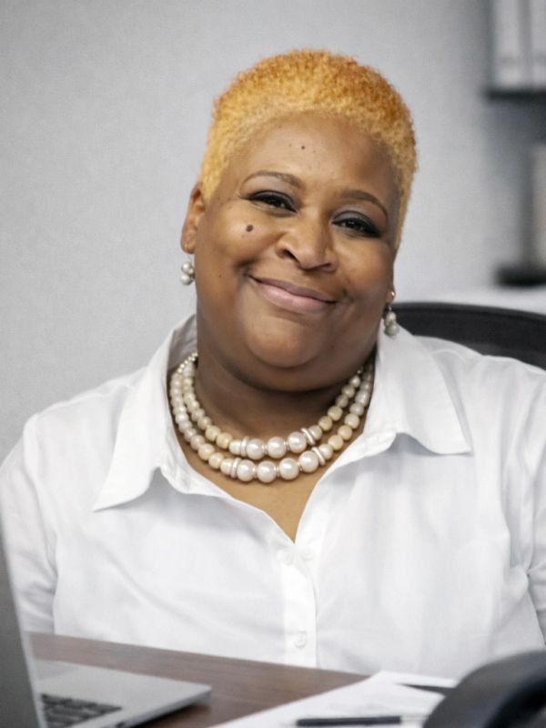 Smiling woman with blonde hair and pearl necklace in white shirt.