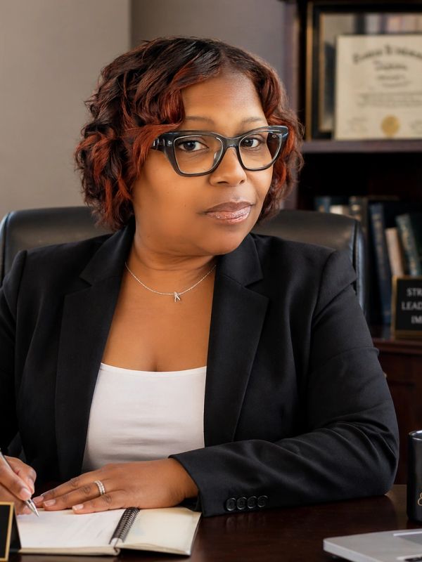 Professional woman in glasses writing in a notebook at her desk.