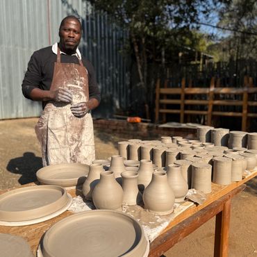 Man working with pottery outdoors, surrounded by clay pots.