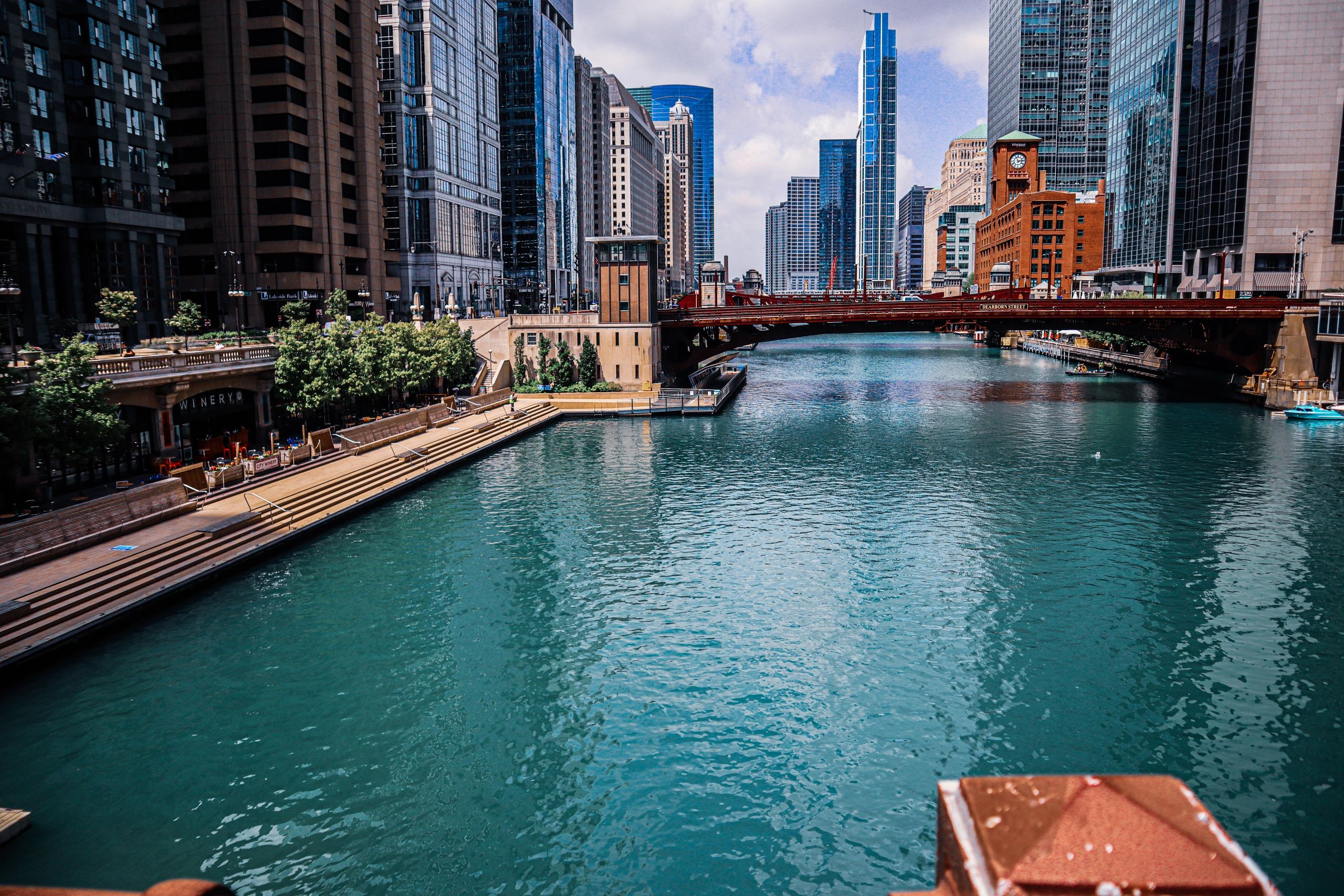 Urban river scene with modern buildings and a red bridge.