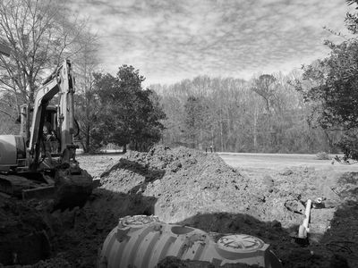 Excavator digging a large hole with a septic tank installation in progress.