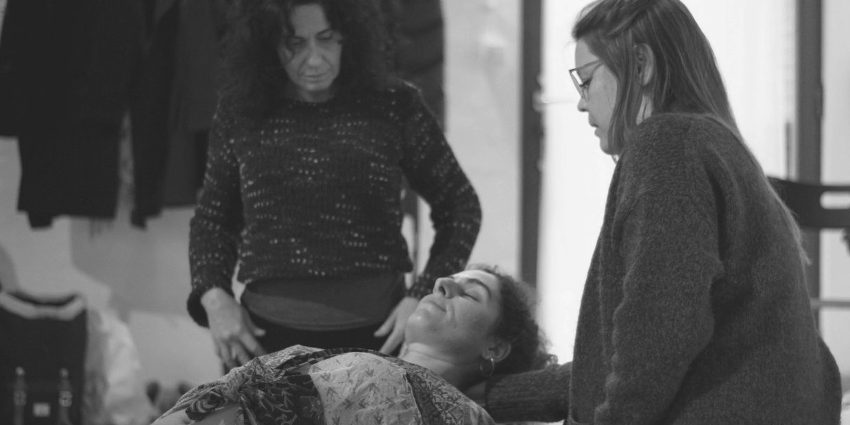 Two women support a reclining woman in a calm indoor setting.