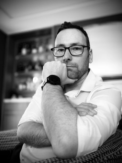 A man with glasses and a smartwatch poses thoughtfully indoors.