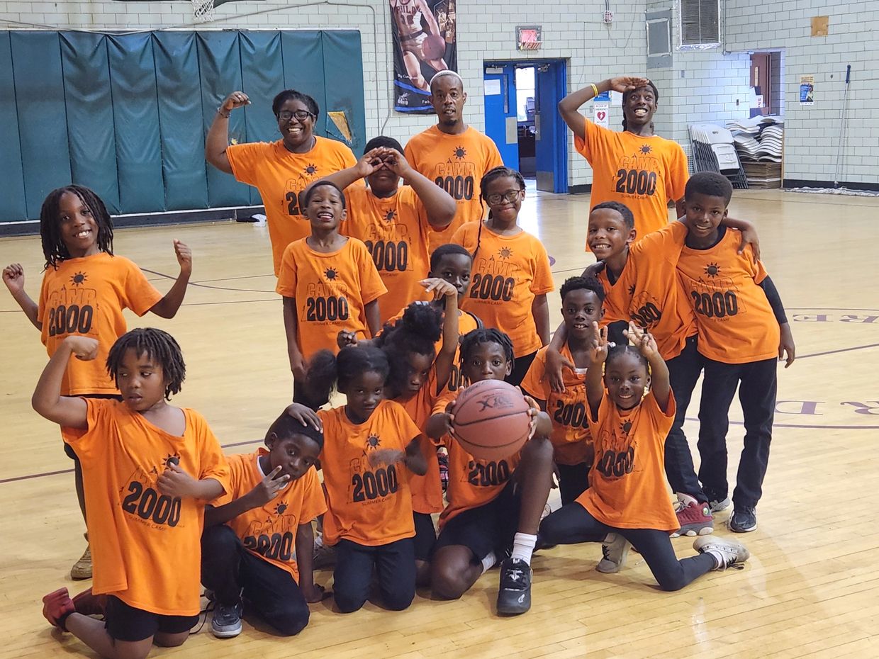 Group of kids and adults in orange camp shirts posing in a gym.
