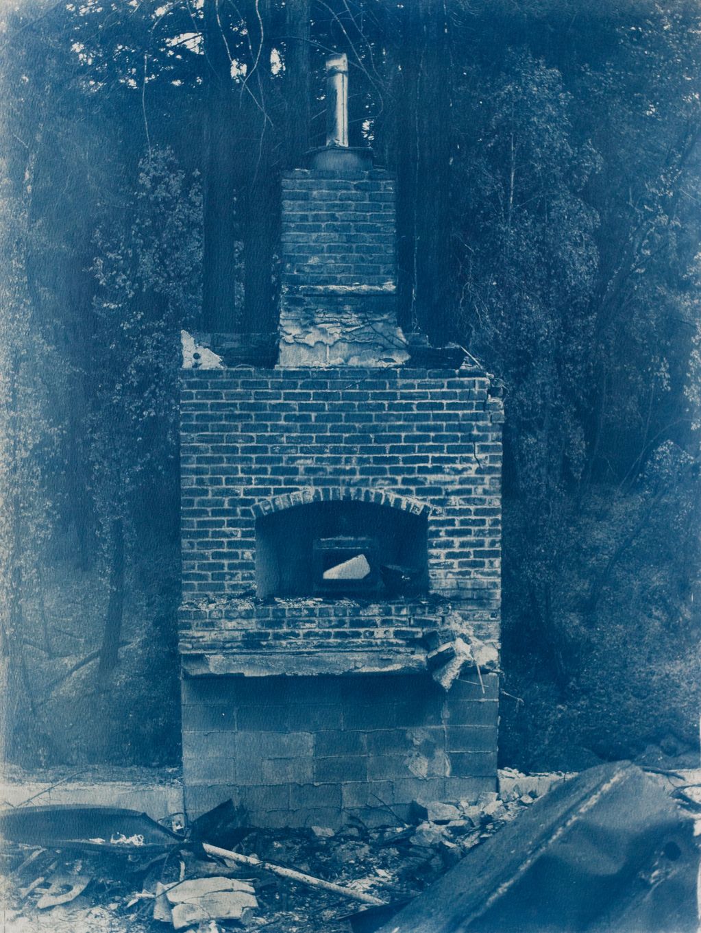 Old, damaged brick outdoor fireplace surrounded by debris in a wooded area.