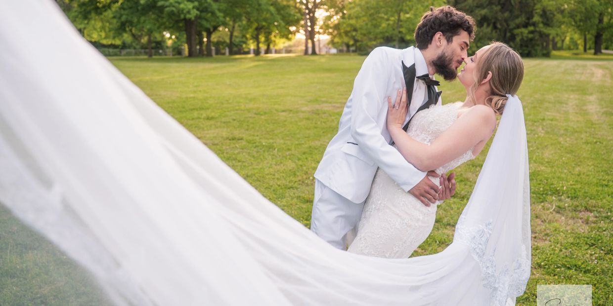 Bride and groom share a romantic moment in the park with a flowing veil.