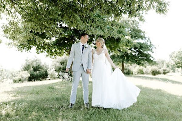 Bride and groom holding hands under a large tree on their wedding day.