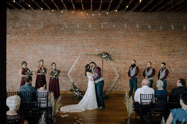 A couple shares a kiss during their wedding ceremony in a rustic venue.