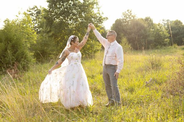 Couple dancing outdoors in wedding attire during golden hour.
