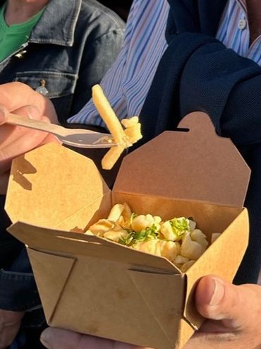 A man smiling, holding a box of poutine with a fork in hand