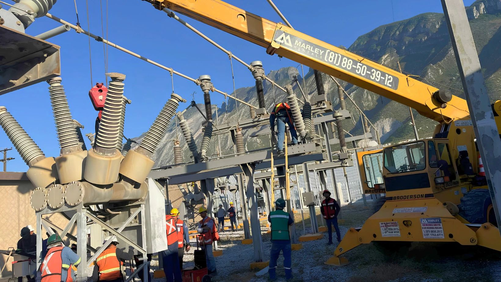 Trabajadores reparando equipo eléctrico con grúa en zona montañosa.