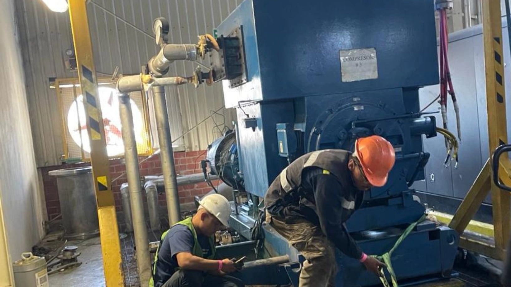 Trabajadores con cascos trabajando en maquinaria industrial.