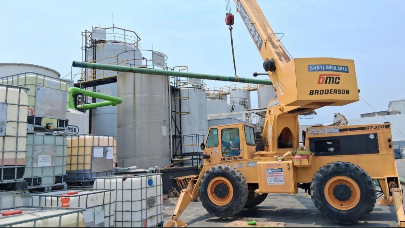 Grúa amarilla en planta industrial con tanques y contenedores.