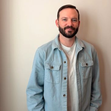 Man smiling in a light blue jacket and white t-shirt.