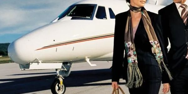 A stylish couple walking beside a private jet on a sunny day.