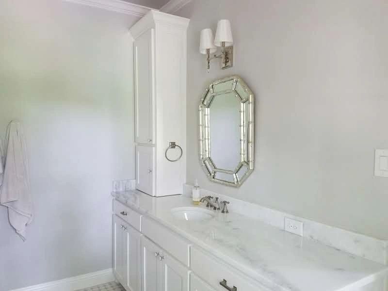 Bright bathroom with white cabinetry, marble countertop, and an elegant mirror.
