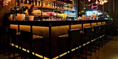 Dimly lit bar with high stools and warm lighting under the counter.