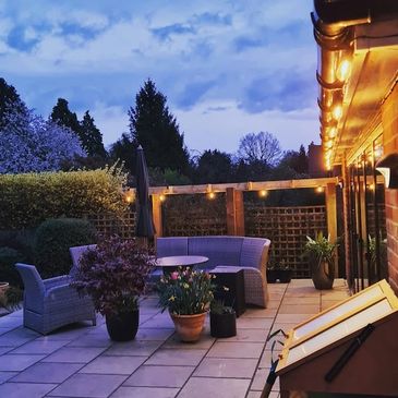 Cozy illuminated outdoor patio with wicker furniture and greenery.