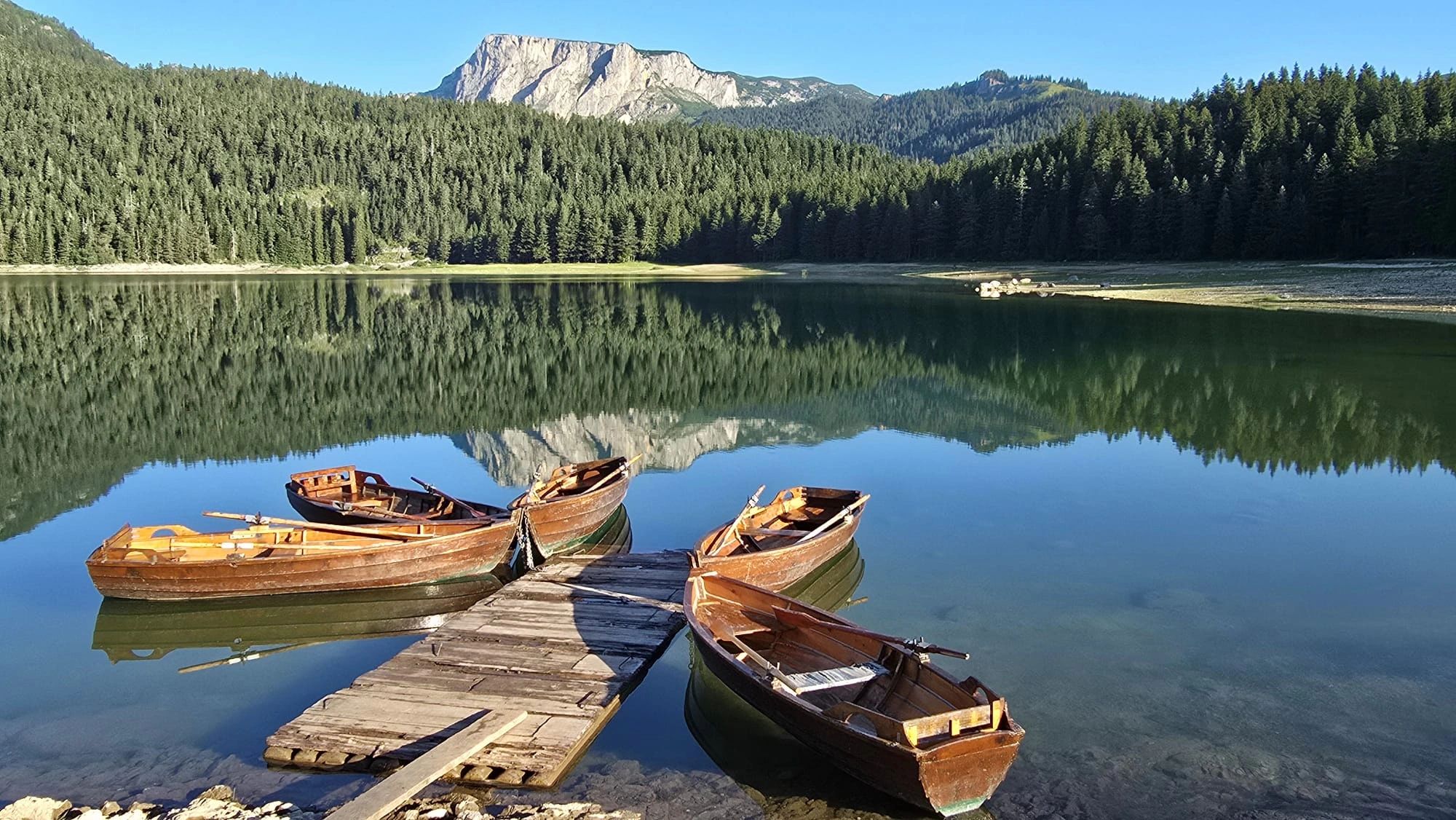 Rows of wooden boats on a calm lake with mountain reflection.