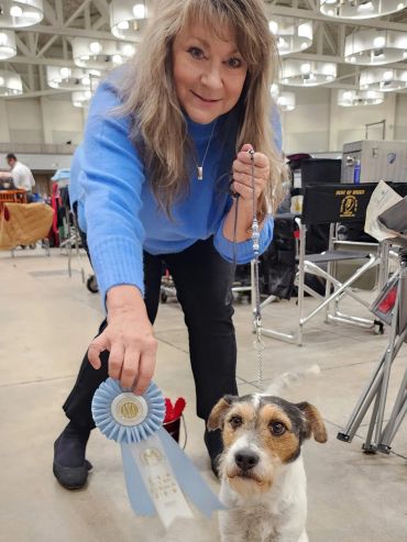 Woman proudly displays blue ribbon with her dog at a competition.